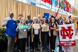 Eleven adults pose as a group while holding merchandise from the different universities they represented at the symposium.