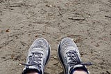 A runner’s feet on sand wearing grey running shoes