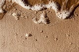 Close-up of beach: sand, line of foam encroaching from the top of the photo