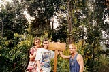 Three travelers stand by a sign in a forest area, directing hikers to Bukit Lawang, Sumatra.