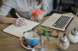 girl writing in notebook near a laptop