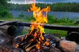 Campfire on a beach next to a lake with a forest in the background