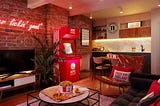 The KFC hotel room features a neon sign “it’s finger lickin’ good”, aa House of Harland cushion, a big TV, kitchen, sofas and of course a bucket of chicken