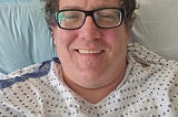 author in the hospital with a smile on his face, wires coming out of his chest, and killer curly hair