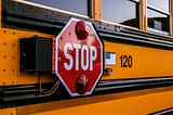 A close up of the Stop sign on the side of a yellow-school bus.