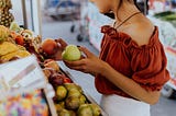 Young woman holding a green apple and an orange in the super market