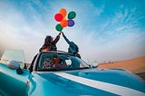 Two women release balloons into the sky on a dusty road