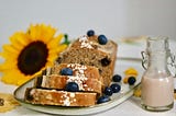 A vegan banana bread with blueberries, a glass of milk and a sunflower for decoration