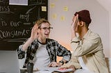 Two men sitting on a table with open books and about to high-five.