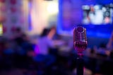 An old-fashion microphone is in the foreground, behind is an office bathed in blue light.