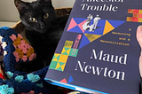 Black kitten in basket on a vest croched with granny squares, and a book