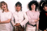 Four women with punk outfits and hairdos and irreverent facial expressions