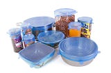 several bowls, cans, and other food containers covered with stretchy silicone lids