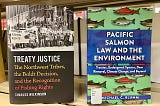 Two books sit side by side on a shelf. They are shown with their covers out. The book on the left is titled, “Treaty Justice: The Northwest Tribes, the Boldt Decision, and the Recognition of Fishing Rights.” The book on the right is titled, “Pacific Salmon Law and the Environment.”