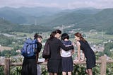 4 young women who are sisters in an embrace looking upon a vast spread of mountains and grasslands.