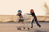 A kid pushes another kid in a supermarket trolley