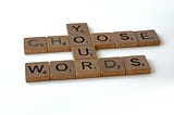 A series of square tiles with letters and numbers, reminiscent of the game Scrabble. These tiles are arranged against a stark white background. They spell out the phrase “CHOOSE WORDS” in a cascading manner, where each word begins one tile lower than the last letter of the word above it. Each tile bears a single letter in a bold, black font, accompanied by a small number in the corner, indicating the letter’s point value.