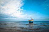 Small blue, yellow and white fishing boat in the ocean, blue sky with some clouds