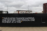 A wall with “This is how change happens. One gesture. One Person. One moment at a time” written on it for people to see.