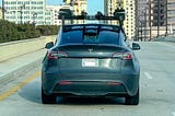 A grey Tesla seen from the rear with a large roof-mounted rack holding a lidar sensor array.