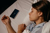 Face and arms of a sleeping woman with a cell phone near her hand.