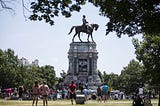 People in a park look at a graffiti-covered statue of Confederate general Robert E Lee on a horse.