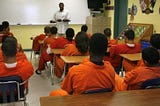 Image of a teacher instructing a full class of incarcerated students in a prison classroom.