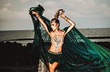 Persian belly dancer holding a green veil dancing on a beach by the sea.