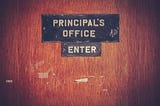 A wooden door with a sign that says “Principal’s Office: Enter”