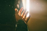 A hand reaching out for help towards a light in a dark room.