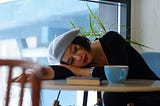 Woman with her head resting on her arm, at a cafe table.
