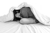 A young woman hiding under her bedcovers riddled with anxiety.