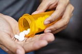 A man pours pills into his hand from an orange prescription bottle