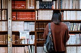 Woman Wearing Brown Shirt Carrying Black Leather Bag on Front of Library Books