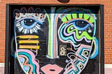 Painted face graffiti on a black door set into a brick wall