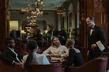 A server at a fancy restaurant dressed in a suit addresses a group of four people sitting around a table