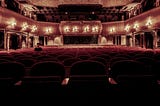 A dimly lit auditorium of a theatre with one man sitting on the left side.