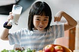 A girl flexes her muscles while drinking a cup of milk.