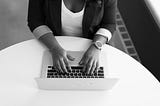 Black in white photo of woman typing on her Macbook.