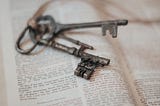 A pair of vintage grey keys on top of an open bible
