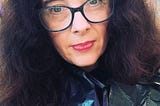 A woman with wild curly brushed put hair wearing glasses and red lipstick