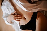 A woman reclined on a bed, her shirt open, revealing her navel.