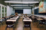 an empty classroom with desks organized into rows facing a black chalkboard