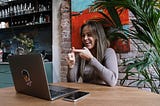 Woman smiling and signing while facing a laptop in a cafe