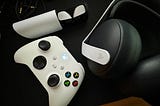 Sony Pulse Explore earbuds and a Pulse Elite gaming headset on a desk next to a powered-on Xbox controller.