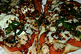 An image of pizza topped with tomatoes, mushrooms, ricotta cheese, bell peppers, basil and red pepper flakes.