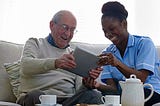 Home care aide shows elderly man how to use an ipad
