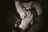 An aged person holding on to the hand of a baby. This picture depicts age