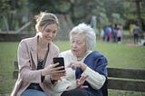 Young woman and old woman looking at a mobile phone at a park