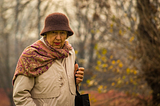 Photo of an old lady in a hat and raincoat on an autumnal day